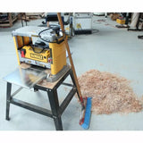 Benchtop wood planer on stand with shavings and broom in woodworking shop