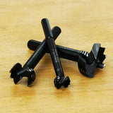 Three black woodworking forstner drill bits on a light wood surface