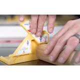 Hand using a yellow woodworking gauge tool to measure a round wooden dowel on a workbench.