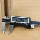 Digital caliper measuring wood thickness at 13.00 mm on a workbench