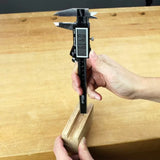 Digital caliper measuring wooden block thickness on woodworking bench