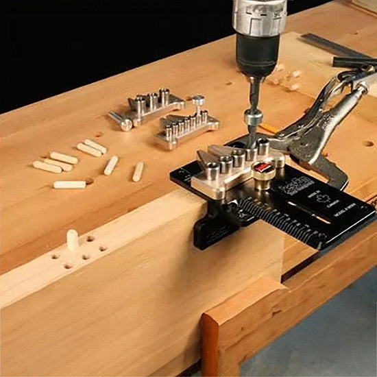 Woodworking dowel jig clamped to wood, with drill and dowel pins on workbench