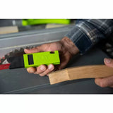Person holding a green woodworking featherboard tool near a saw blade and curved wood piece