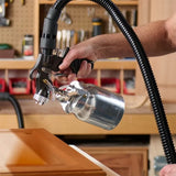 HVLP paint sprayer applying finish to a wooden cabinet door in a woodworking shop