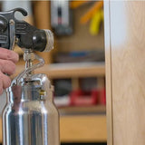 Close-up of a handheld HVLP paint sprayer in a woodworking shop setting.