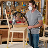 Man wearing safety mask using HVLP spray gun to finish a wooden chair in a woodworking shop