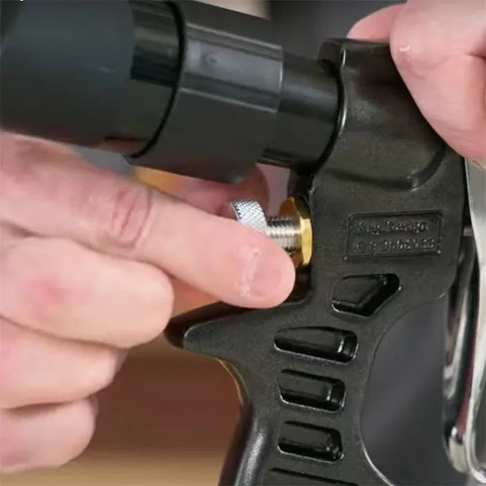 Hand adjusting metal knob on woodworking spray gun nozzle close-up