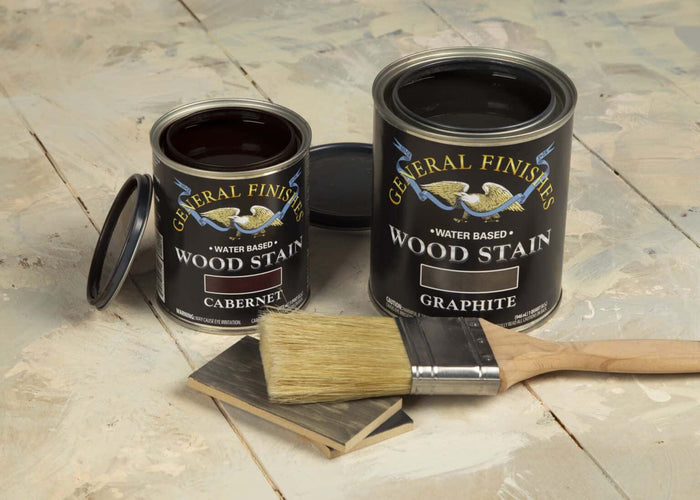 Open cans of water-based wood stain in cabernet and graphite colors with paintbrush and wood samples