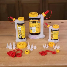 GlüBot, HighBot, and BabeBot glue applicator bottles with assorted caps and tips on a wood table