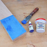 Blue wood grain filler applied to wood with putty knife, filler container, and glue bottle