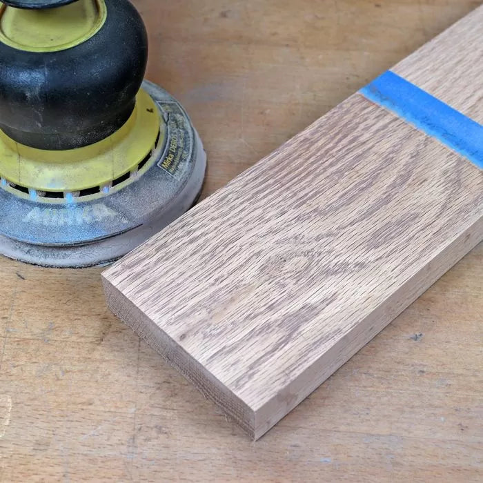 Orbital sander next to sanded hardwood board on workbench, woodworking tools setup