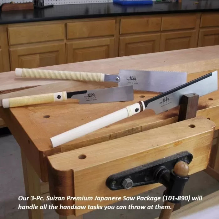 Three Japanese-style woodworking saws with white handles displayed on a woodworker's bench in a workshop.