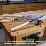 Three Japanese-style woodworking saws with white handles displayed on a woodworker's bench in a workshop.
