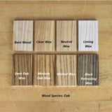 Oak wood samples showing finishes: bare, clear wax, neutral wax, liming wax, dark oak, medium oak, walnut, and black patinating wax on a wooden table.