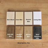 Comparison of pine wood finish samples showing effects of bare wood, clear wax, neutral wax, liming wax, dark oak wax, medium oak wax, walnut wax, and black patinating wax on a wood surface.