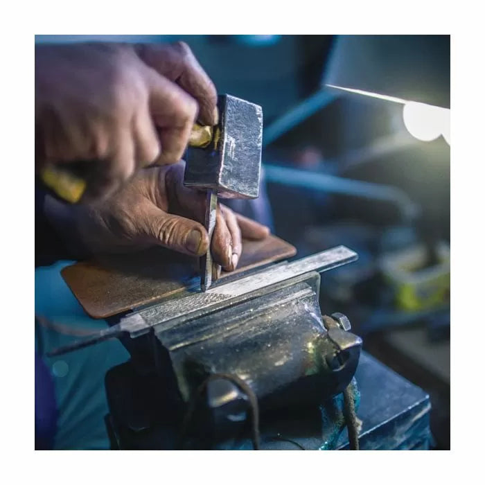 Close-up of hands using a chisel and hammer on metal in a workshop vise