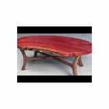Oval live edge coffee table with red wood top and curved wooden legs in a workshop setting.