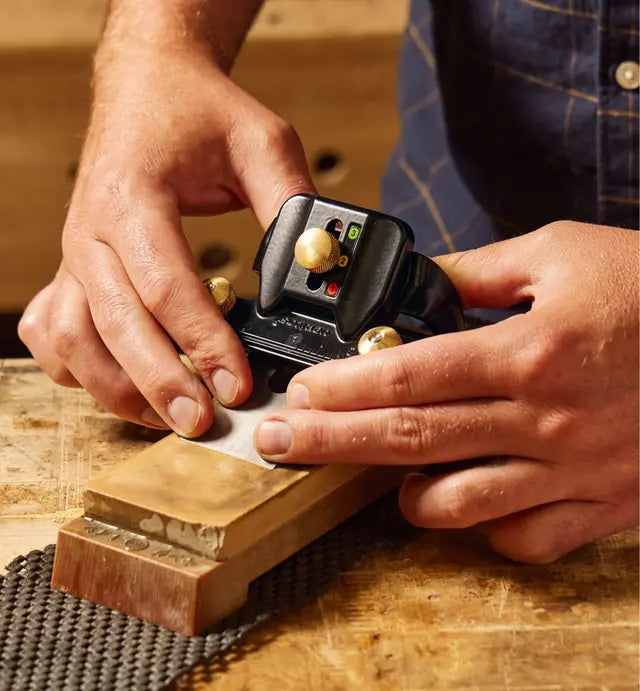 Woodworker sharpening chisel with honing guide on whetstone, woodworking tool close-up