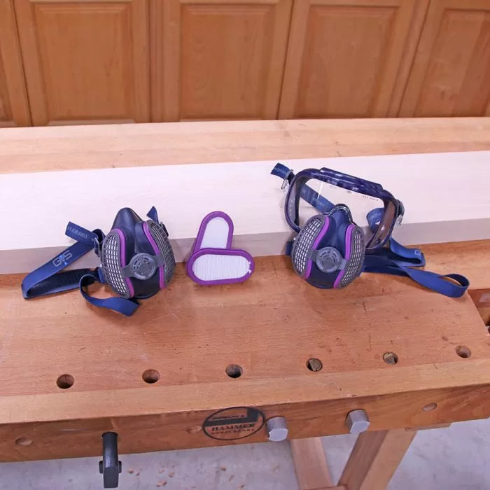 Woodworking respirator masks, safety goggles, and filters on a workbench in a workshop.