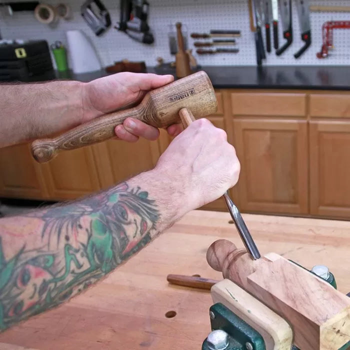 Woodworker using a mallet and chisel to carve a wooden piece in a workshop