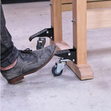 Person using foot pedal to lift workbench on caster wheels in woodworking shop