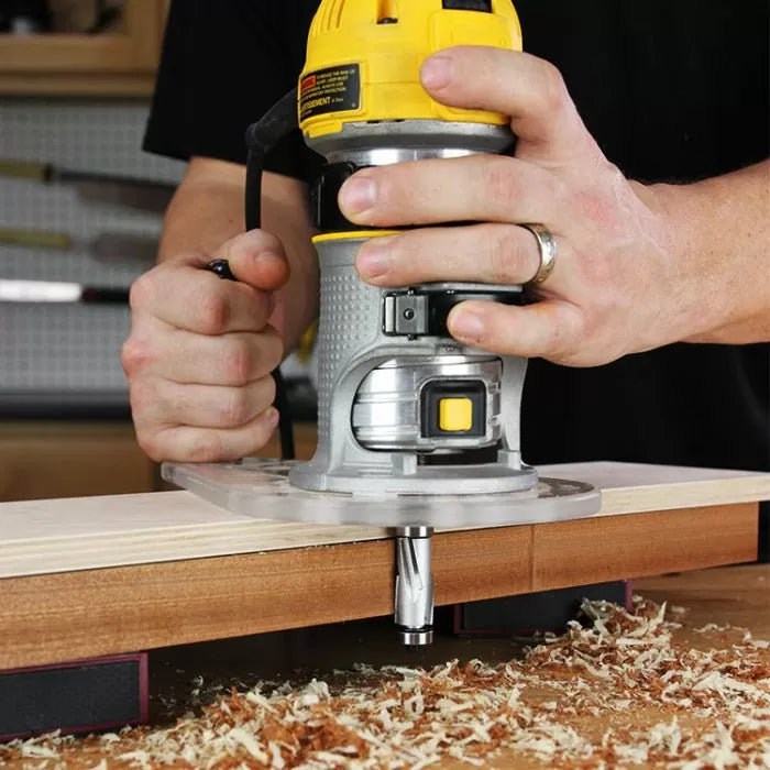 Woodworker using a handheld router with router bit to shape wood edge in workshop