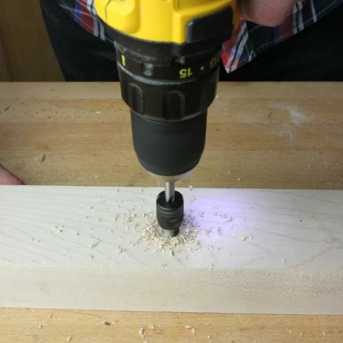 Cordless drill with bit making a hole in a wooden board on a workbench