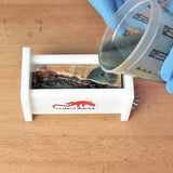 Pouring resin into a woodworking mold with wood blank on a workbench, gloved hand visible.