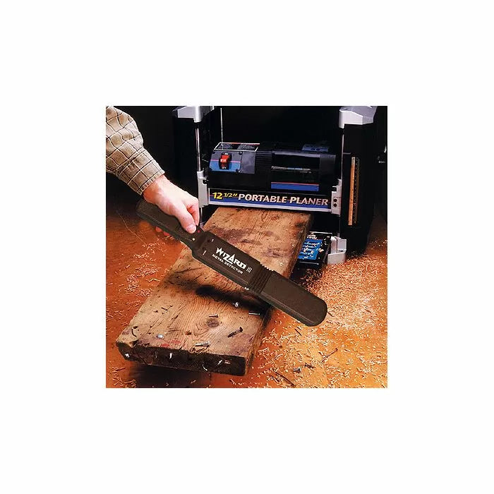 Hand holding Wizard III planer blade jig near portable planer and rough wood board in workshop