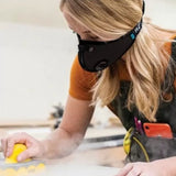 Woman sanding wood in workshop, wearing dust mask for woodworking safety