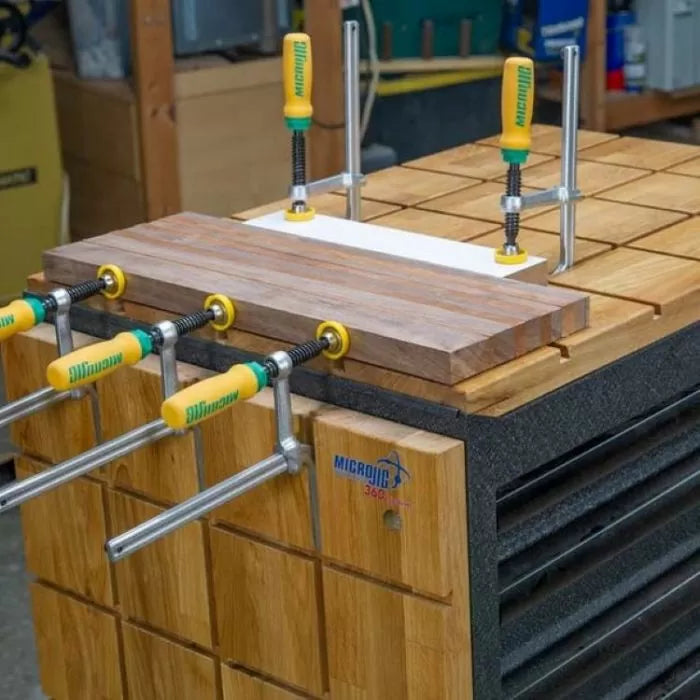 Woodworking jig system clamping boards on a grid workbench in a workshop setting.