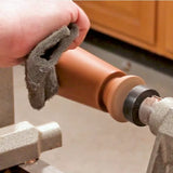 Hand using sanding pad to smooth turned wood piece on lathe in woodworking shop