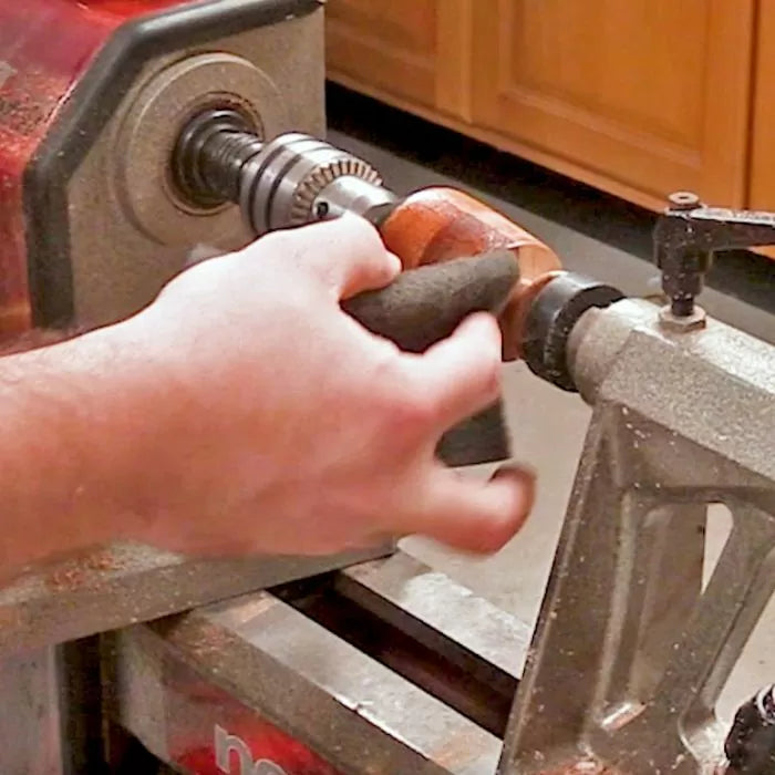 Hand using abrasive pad to sand wood on a lathe in a woodworking shop