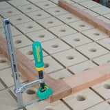 Woodworking clamp securing a board on a perforated workbench, ideal for precise joinery.