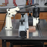 Woodworking router table setup with a hold-down featherboard and fence, workshop background