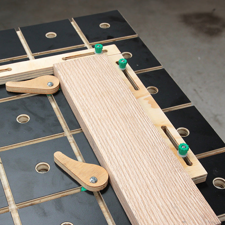 Woodworking bench dog clamps securing a wooden board on a grid workbench