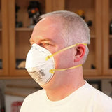 Man wearing N95 dust mask respirator with yellow straps in woodworking shop
