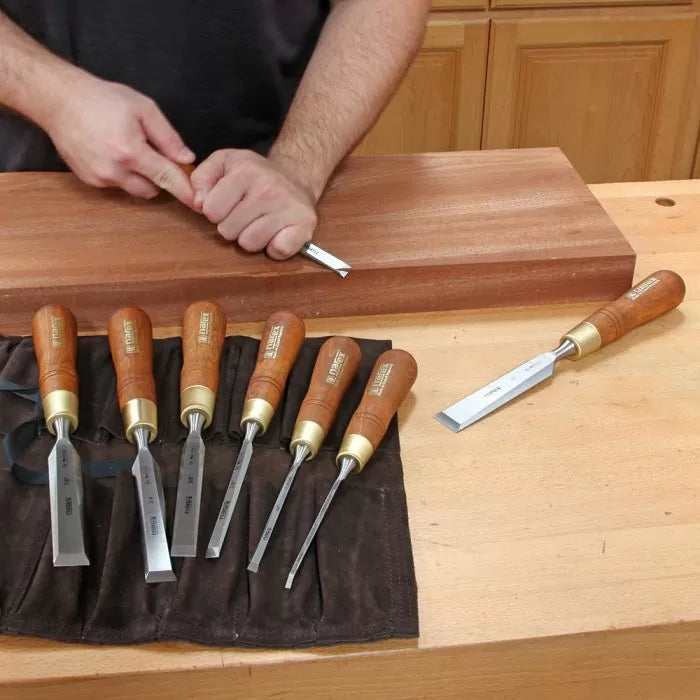 Woodworker using a chisel with a set of six woodworking chisels on a bench