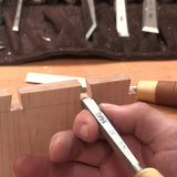Hand using woodworking chisel to clean dovetail joints on wood, woodworking tools in background