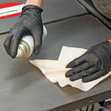 Hands in black nitrile gloves cleaning a table saw surface with spray and paper towel