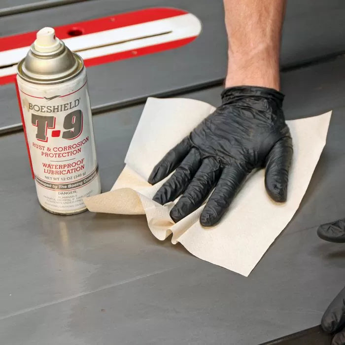 Hand in black nitrile glove cleaning table saw with cloth and rust protection spray