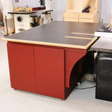 Red woodworking outfeed table with storage cabinets and black work surface in a workshop