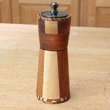 Handcrafted wooden pepper mill with segmented design on a woodworking bench.