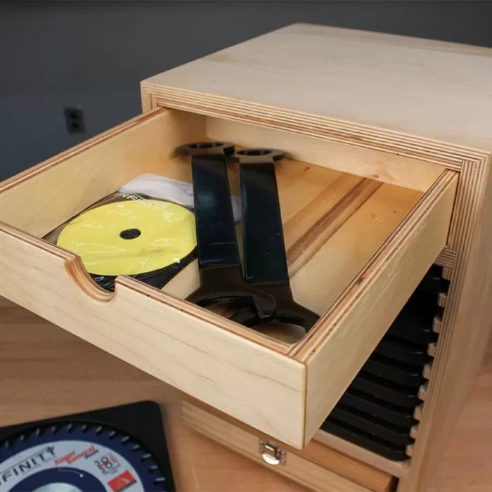 Open wooden drawer storing saw blade wrench and blade accessories in a woodworking shop.