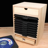 Wooden saw blade storage box with multiple black slots and two drawers on a workbench