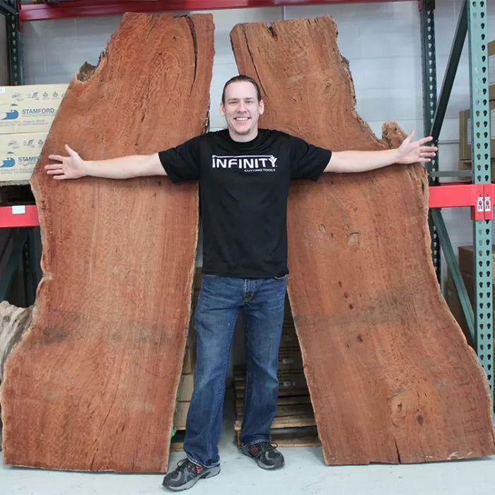 Man standing between two large live edge wood slabs in woodworking warehouse