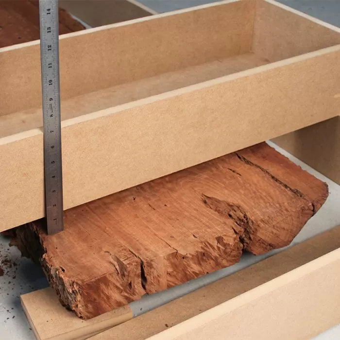 Measuring rough wood slab with a ruler inside a woodworking jig for precise cutting
