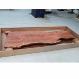 Live edge hardwood slab in a wooden frame on a workshop floor, ideal for woodworking projects.