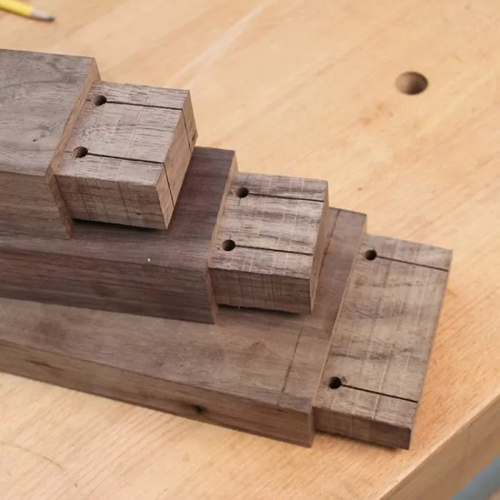 Stacked hardwood blocks with joinery cuts and drilled holes on a woodworking bench