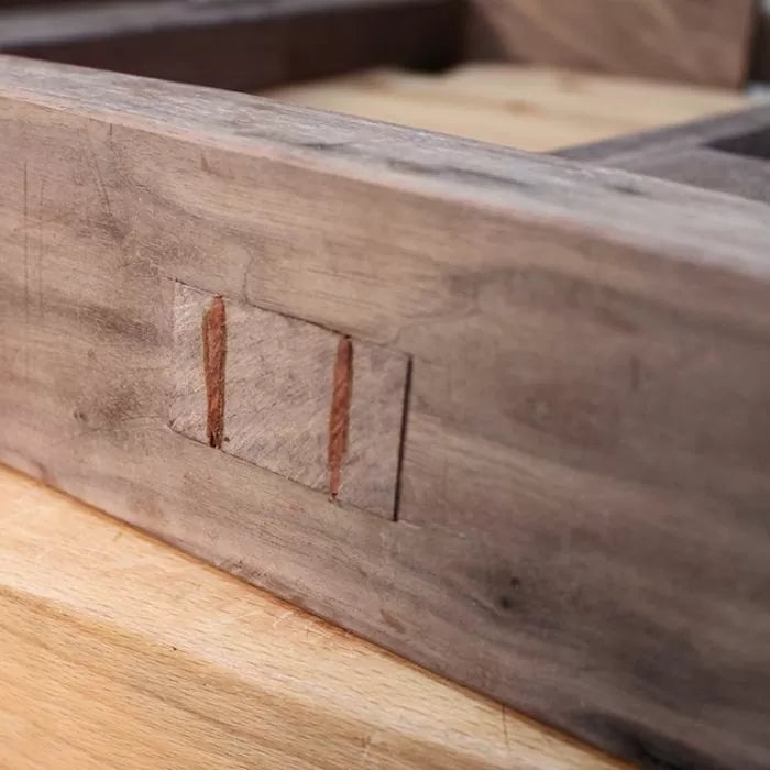 Close-up of a woodworking joint with visible wedges on a wooden furniture frame
